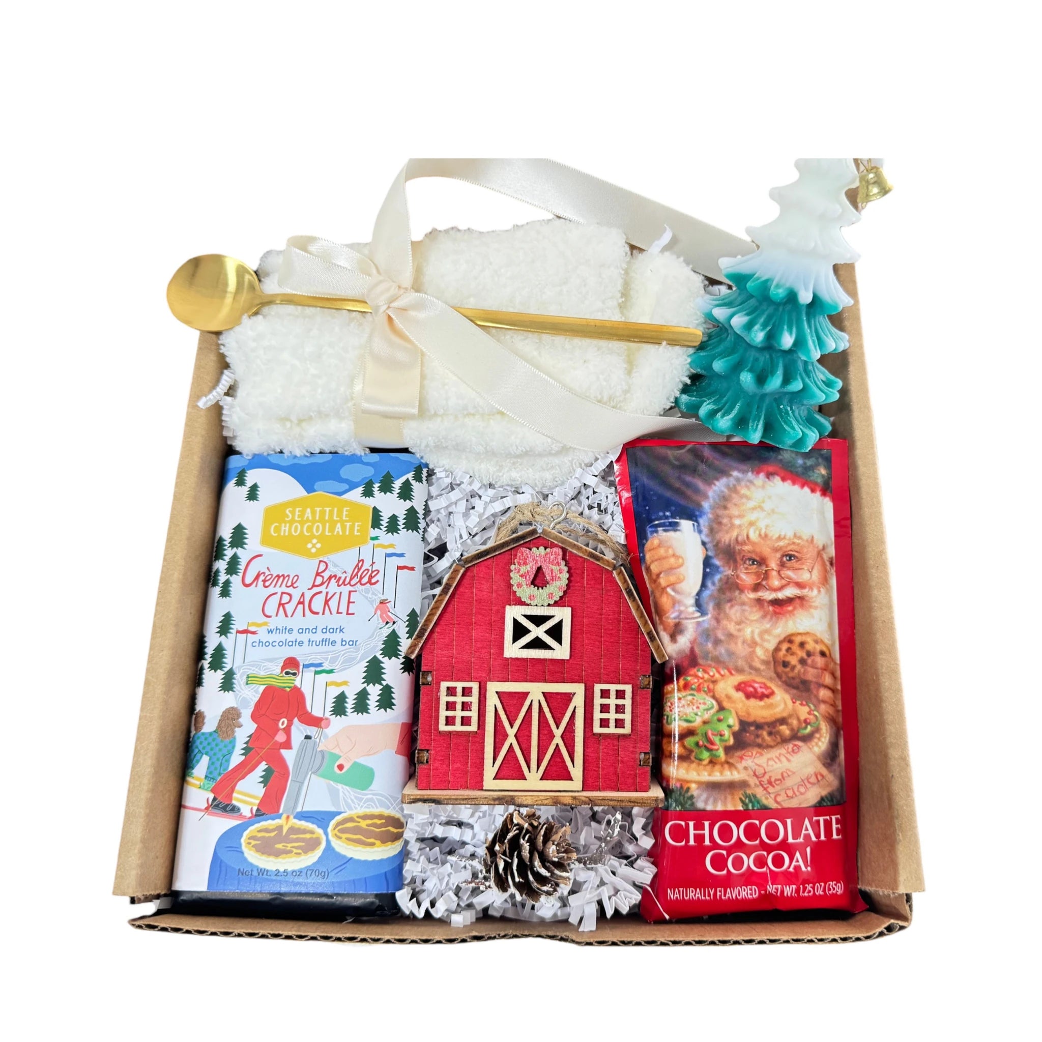 Under My Tree Gift Box featuring white fluffy socks, gourmet chocolate, wooden house ornament, Christmas tree candle, golden coffee spoon, and hot chocolate.