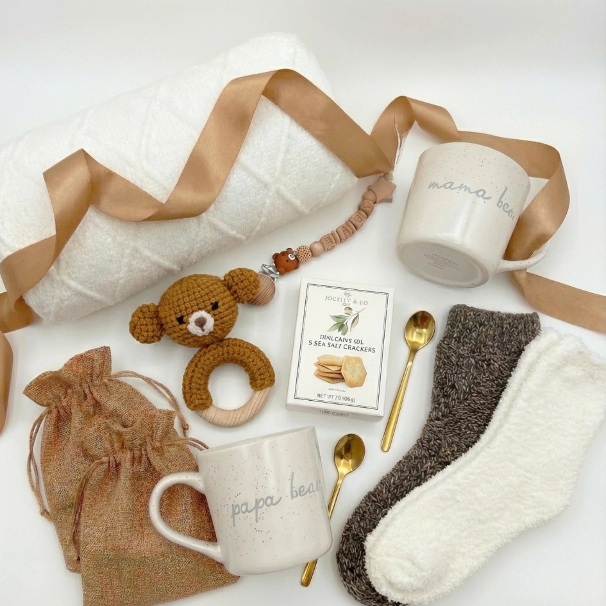 Top down flat lay view of Little Arrival Box items including parent mugs, wooden pacifier clip, teddy bear rattle and gold spoons