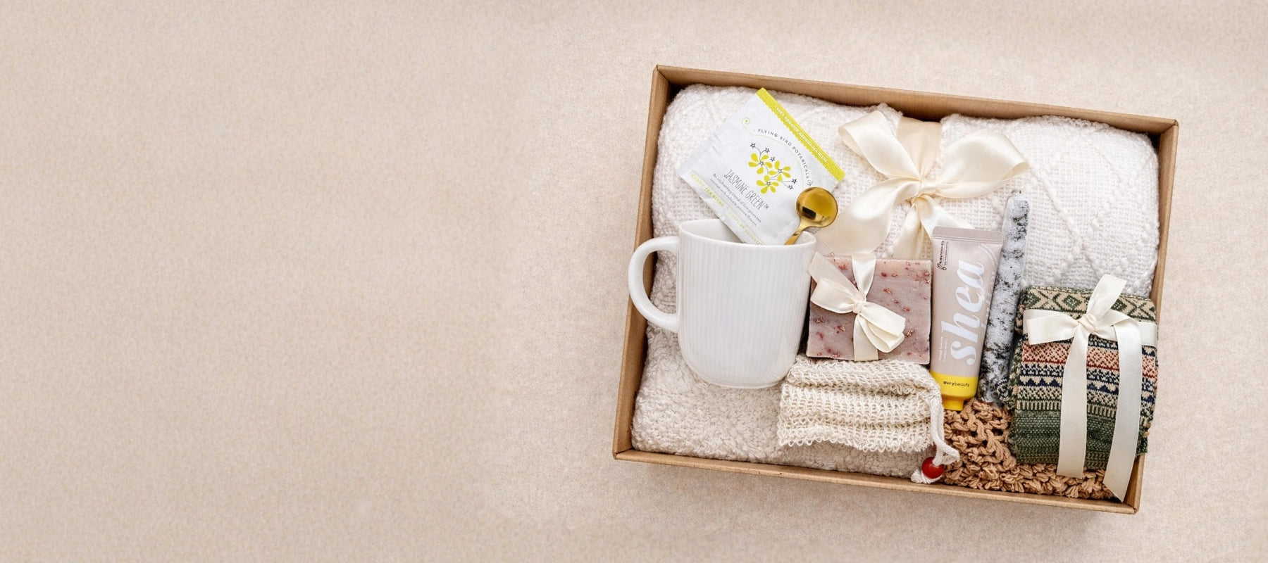 Gift set with a mug, throw blanket and other items in a box on a beige background