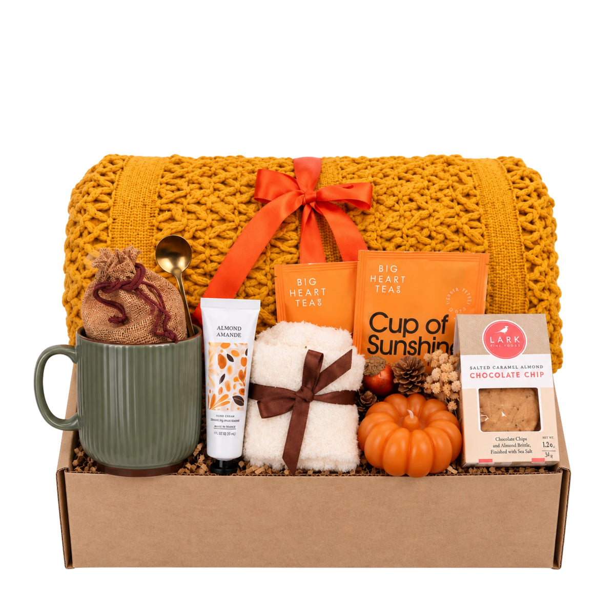 Pumpkin Glow gift box featuring chunky knit mustard blanket, sage green ceramic mug, sculpted pumpkin candle, almond hand cream, fuzzy socks, turmeric tea, and cookies