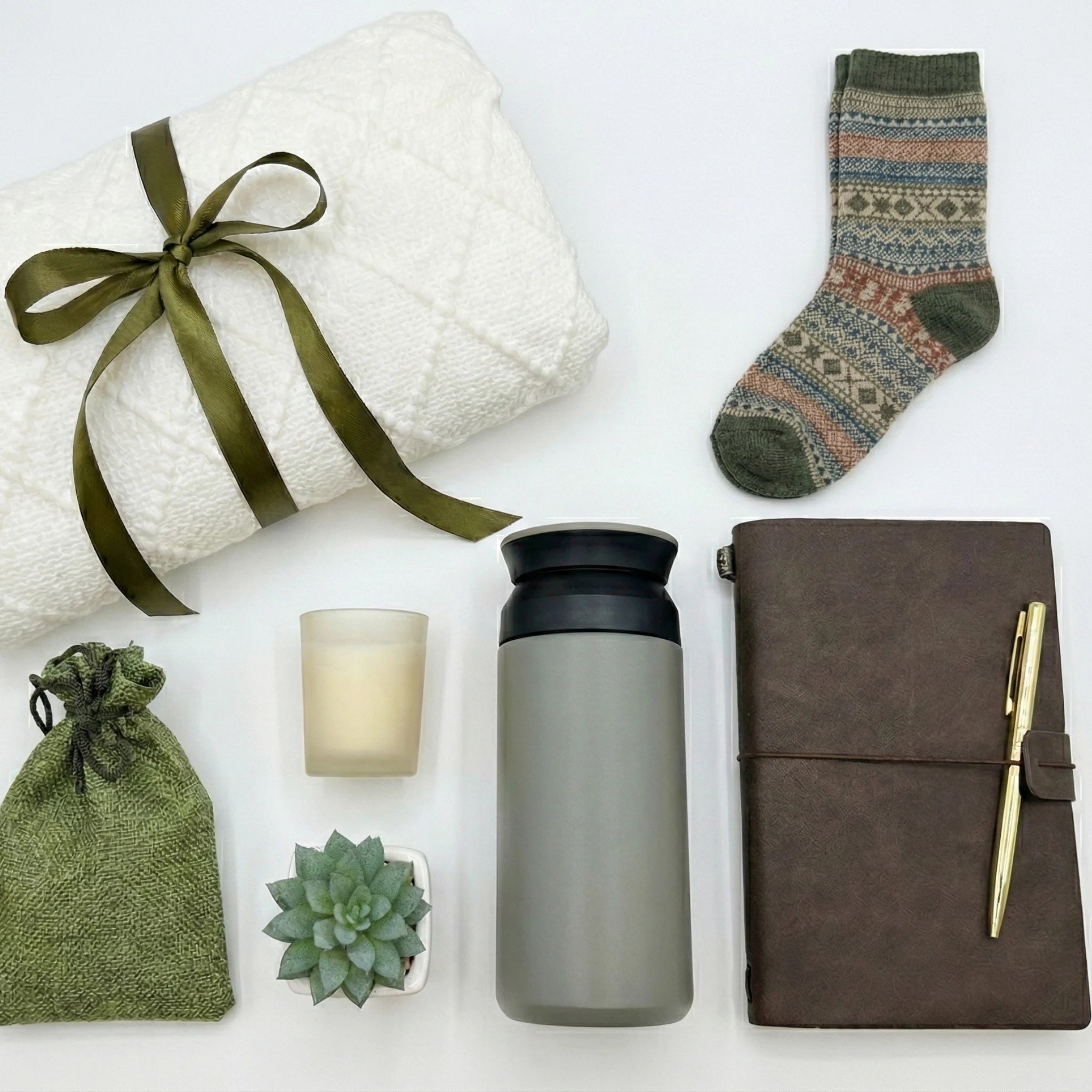 Top down flat lay view of masculine gift box items including grey tumbler and leather journal