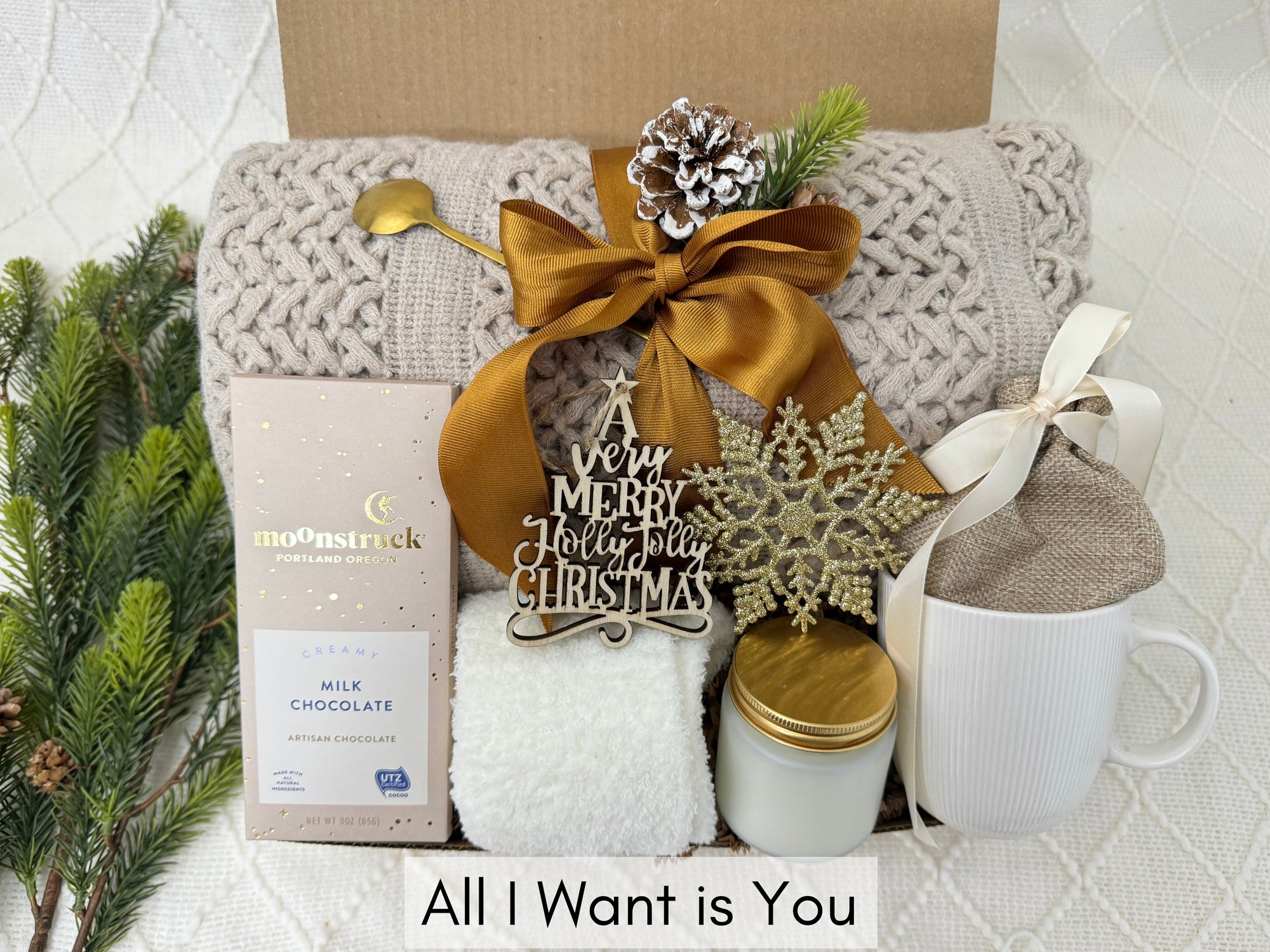 All I Want is You Gift Box by Arinna Gifts featuring a throw blanket, fluffy socks, gourmet chocolate, coffee mug, golden spoon, hot chocolate, candle, and Christmas ornaments.