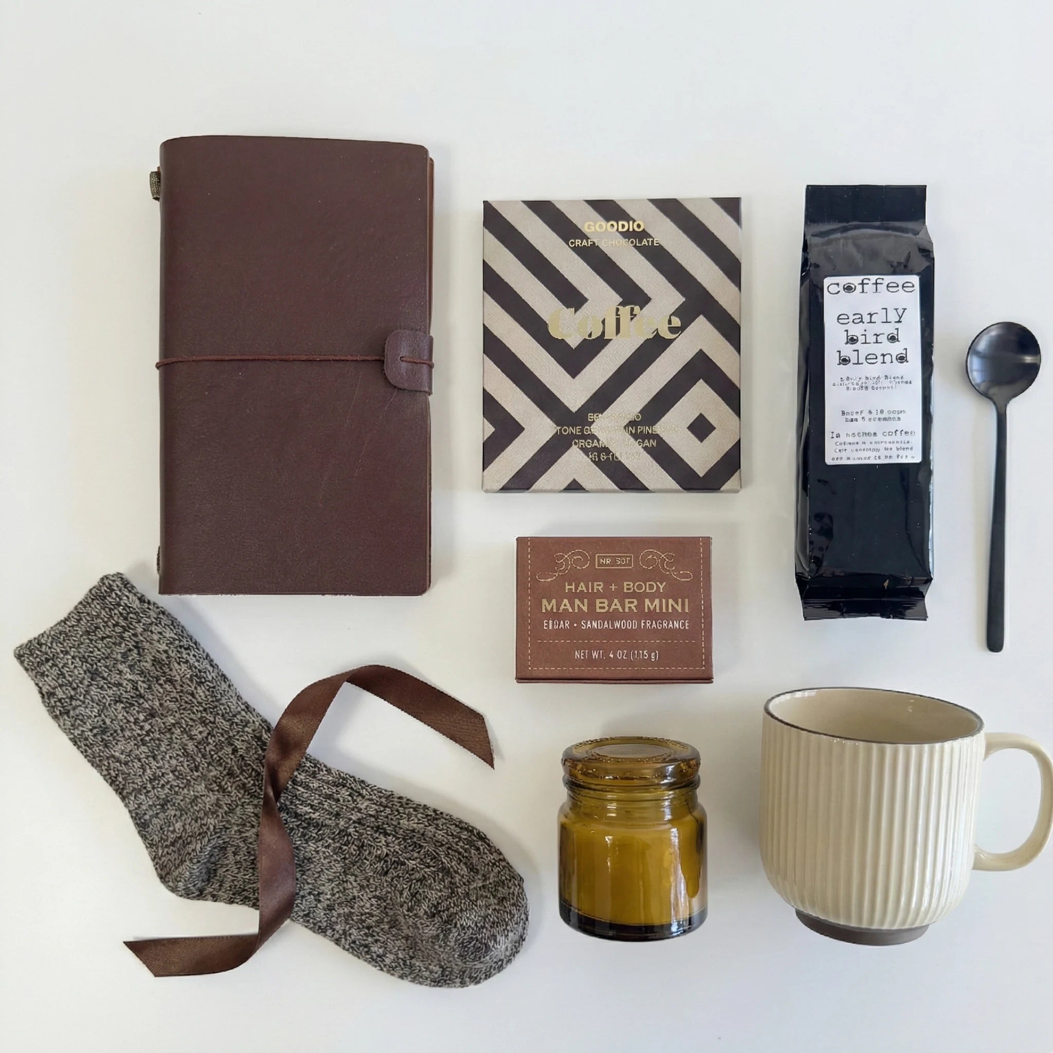 Collection of items including a brown leather notebook, coffee beans, a mug, socks, and a candle on a white background.