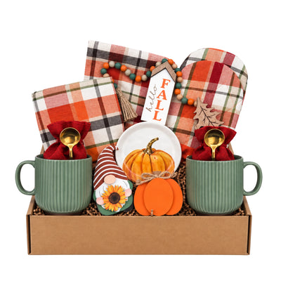 An autumn-themed gift box set containing two sage green ribbed mugs with gold spoons, folded plaid napkins, a small orange pumpkin, a painted gnome, a white plate, and a 'Hello Fall' sign.