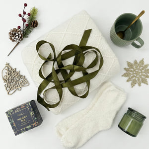 Top down flat lay view of Holly Jolly box items including gold snowflake and green candle