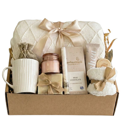 Cozy white throw blanket, mug, candle, socks, chocolate and self-care items arranged in a neutral gift box by Arinna Gifts in Dallas, TX – comforting hug-in-a-box style care package