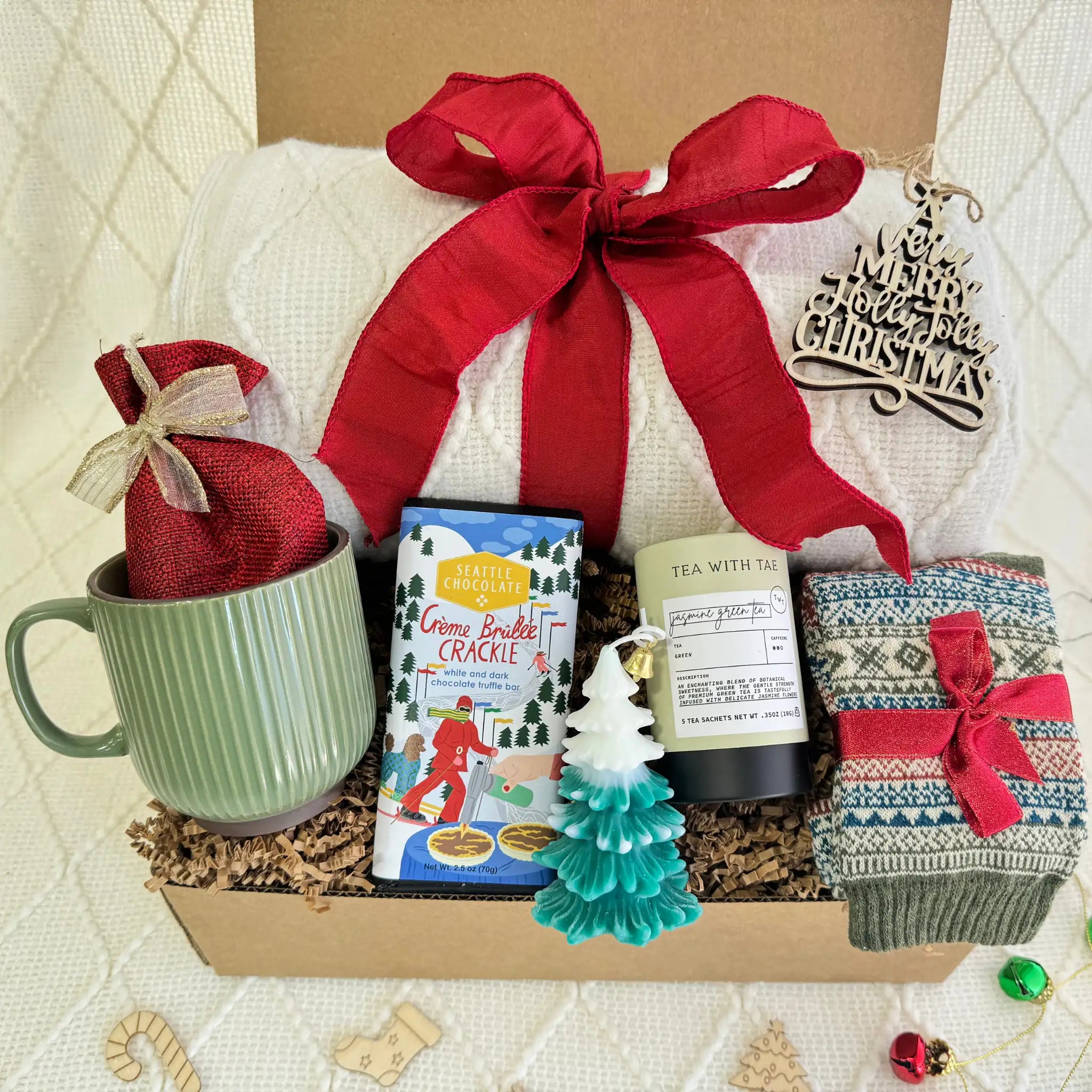 Let’s Stay Home Gift Box by Arinna Gifts featuring a throw blanket, Nordic socks, gourmet chocolate, coffee mug, hot chocolate, candle, herbal tea, and Christmas ornament.