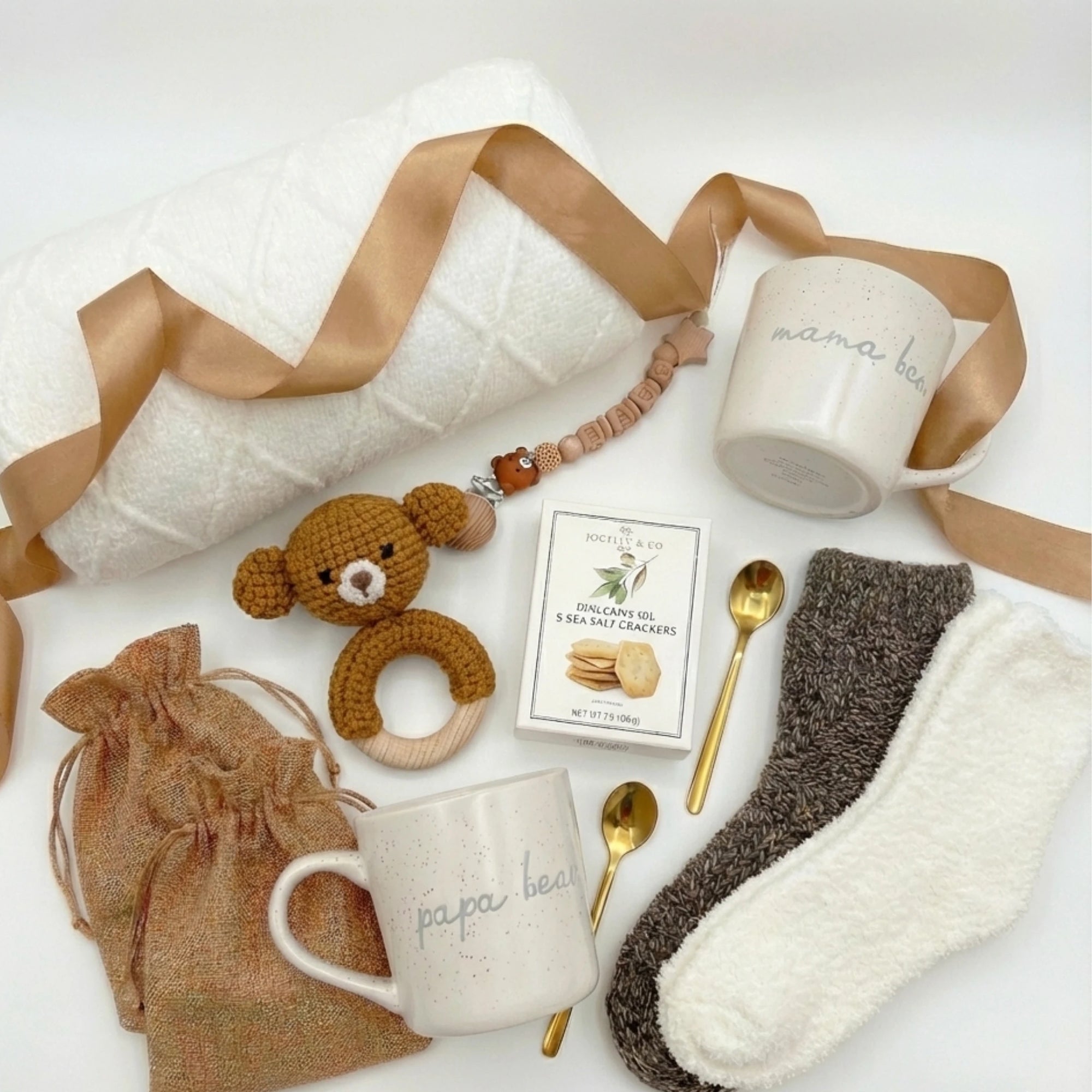 Top down flat lay view of Little Arrival Box items including parent mugs, wooden pacifier clip, teddy bear rattle and gold spoons