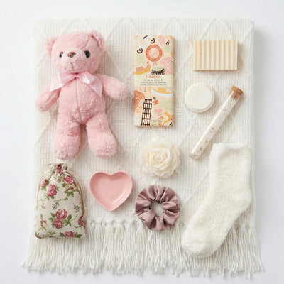 Top down flat lay view of Love You box items including pink teddy bear, heart dish and Tiramisu chocolate