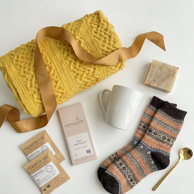 Top down flat lay view of Sending Kisses box items including yellow blanket, tea, and socks hand-packed in Dallas