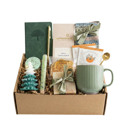 Winter Wonderland Gift Box featuring a pocket notebook, Nordic socks, dried orange slices, coffee mug, gourmet chocolate, herbal tea, handmade soap, bath salt, shower steamer, Christmas tree candle, and golden pen.